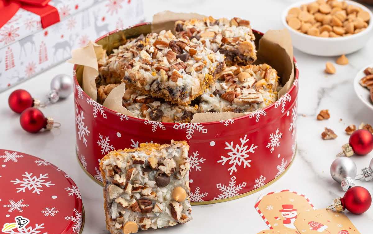 Christmas tin filled with 7 layer bars surrounded by holiday decorations.