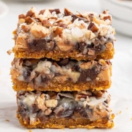 Stack of three 7 layer bars highlighting the gooey chocolate and coconut layers.