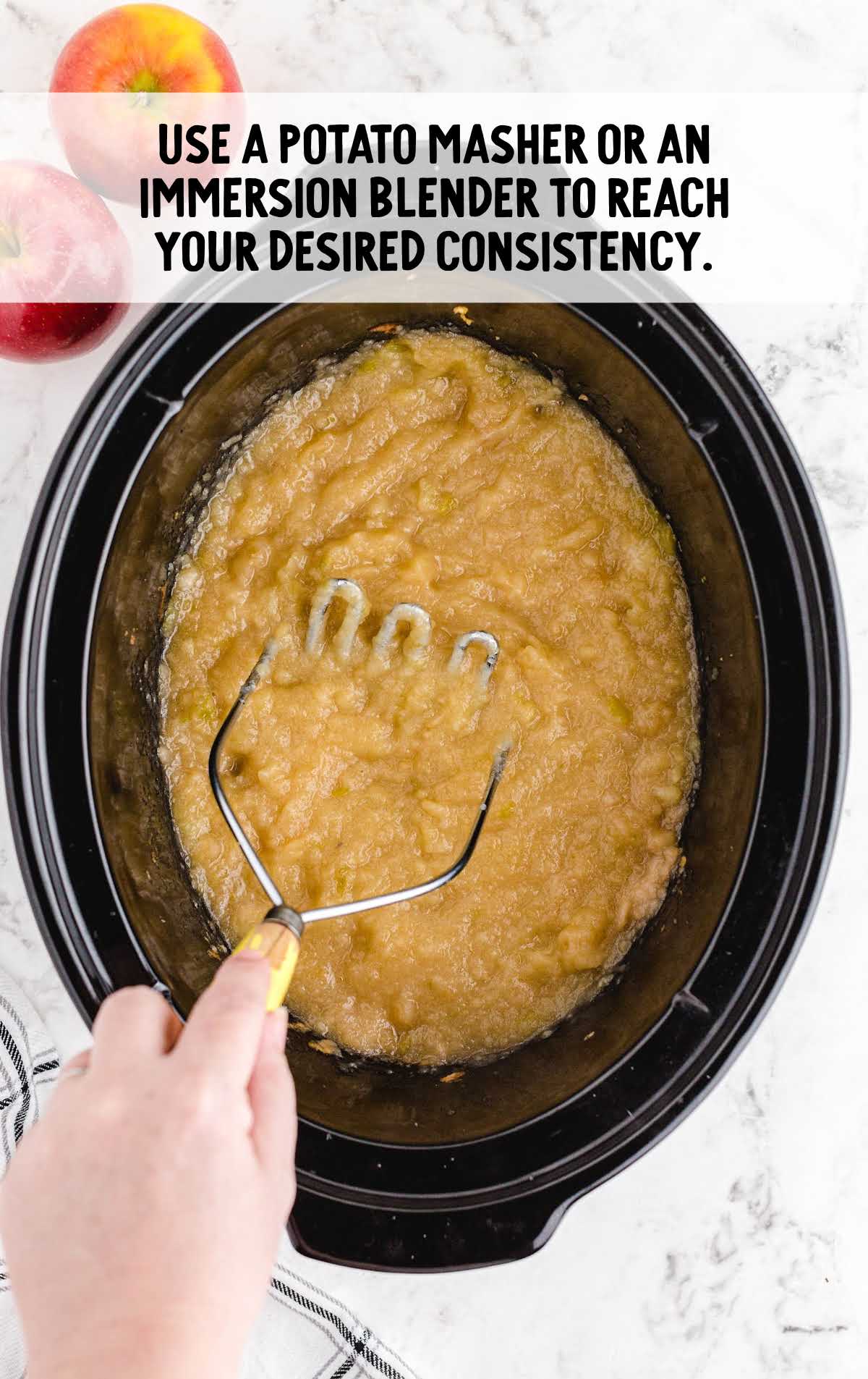potato masher smooshing applesauce in a crockpot