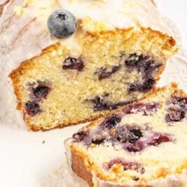 close up shot of a loaf of pound cake topped with glaze and blueberries