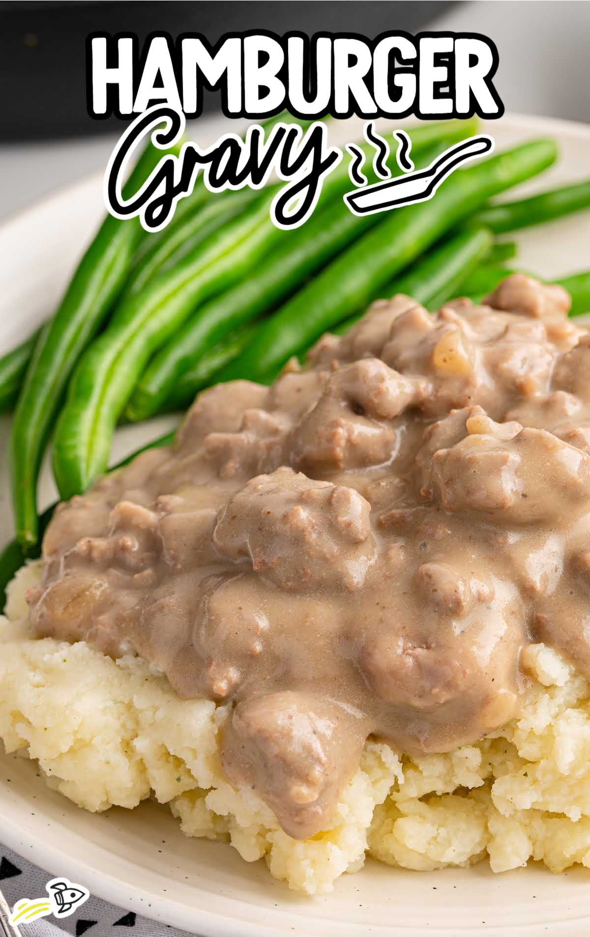 Hamburger gravy spooned over mashed potatoes with vibrant green beans, text overlay reads “Hamburger Gravy.”
