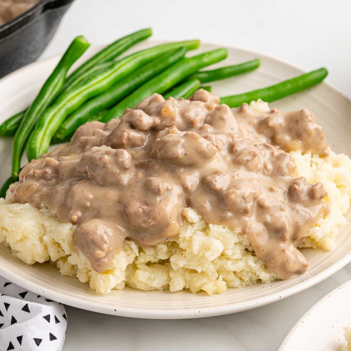 Classic serving of hamburger gravy over mashed potatoes with green beans, styled for a recipe card