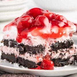 close up shot of a slice of cake topped with cherry pie filling on a plate with Oreos
