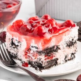 close up shot of a slice of cake topped with cherry pie filling on a plate with a fork