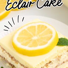a close up shot of a slice of Lemon Eclair Cake on a plate topped with a sliced lemon