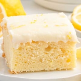 Slice of lemon sour cream cake on a small plate surrounded by fresh lemon slices.