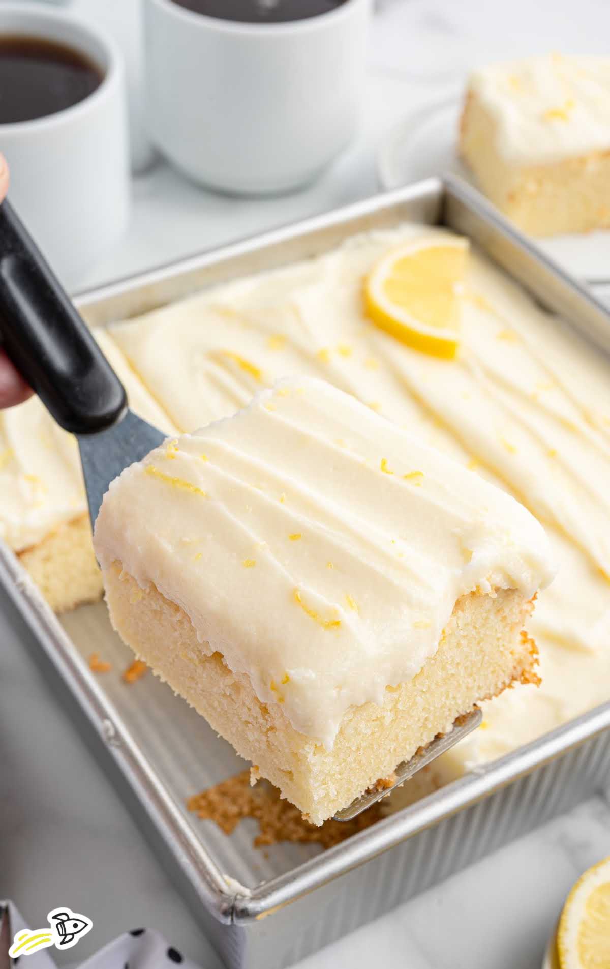 Lemon sour cream cake slice being lifted from a baking pan with a spatula.