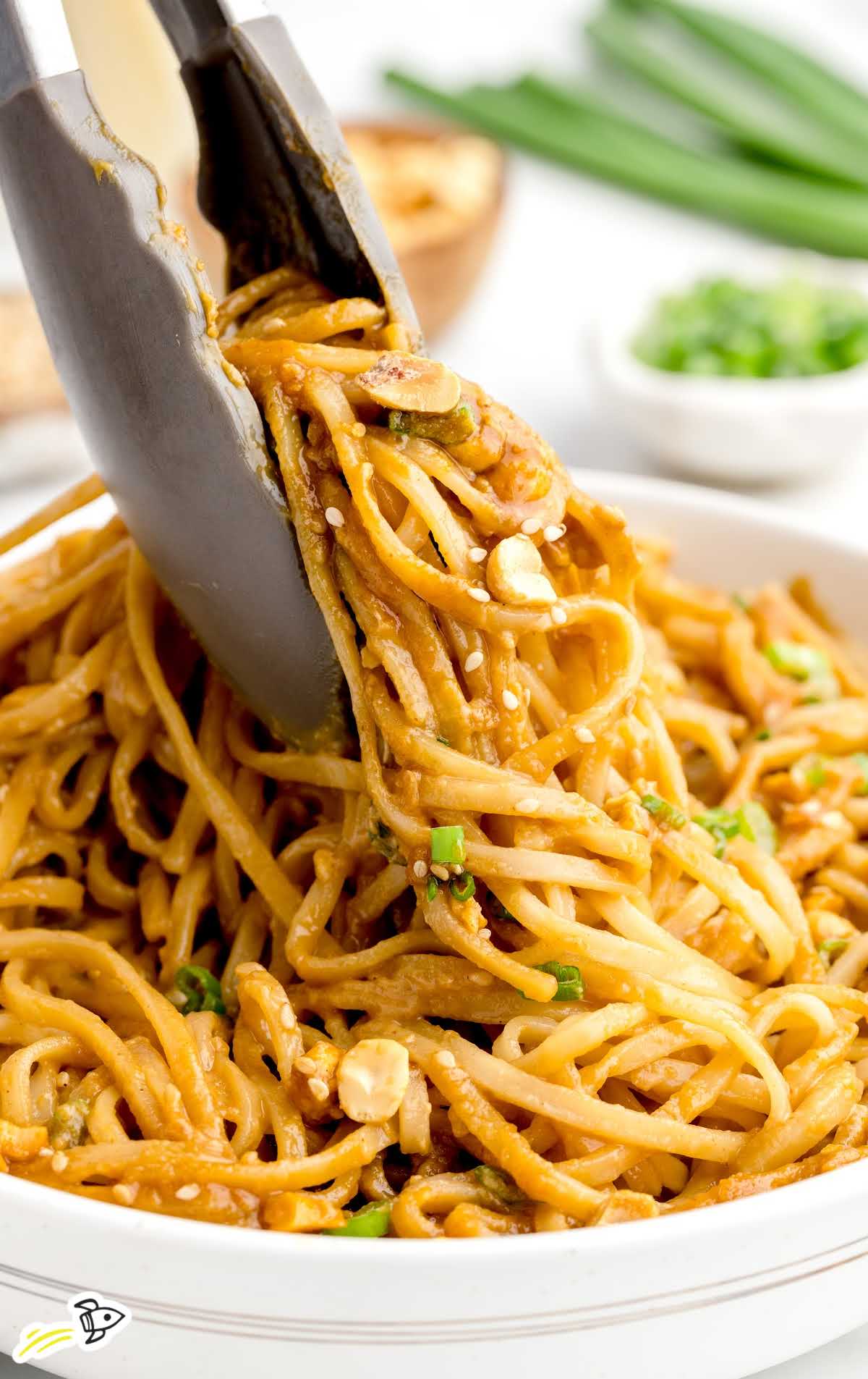 a close shot of Peanut Noodles in a bowl with tongs grabbing a piece
