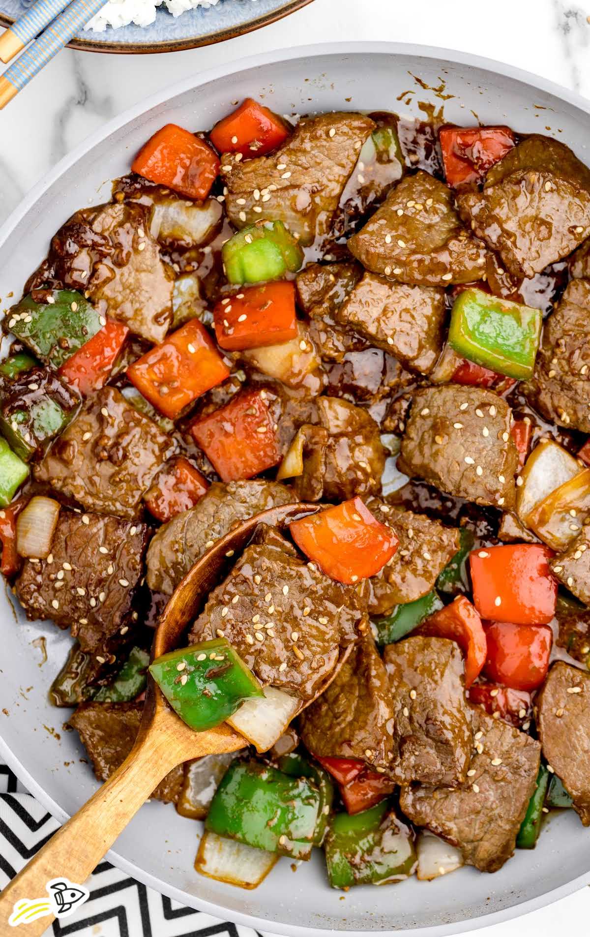 overhead shot of Pepper Steak on a plate with a wooden spoon grabbing a piece