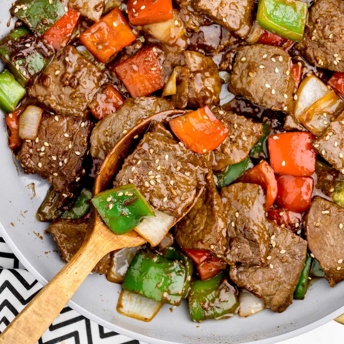 overhead shot of Pepper Steak on a plate with a wooden spoon grabbing a piece