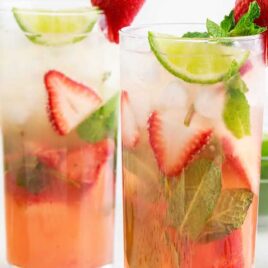 a close up shot of Strawberry Mojitos in a tall glass garnished with sliced strawberries and mint leaves