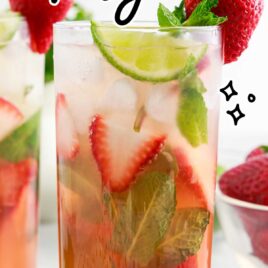 a close up shot of a Strawberry Mojito in a tall glass garnished with sliced strawberry and mint leaves