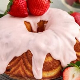close up shot of a cake topped with strawberry glaze and strawberries on a cooling rack