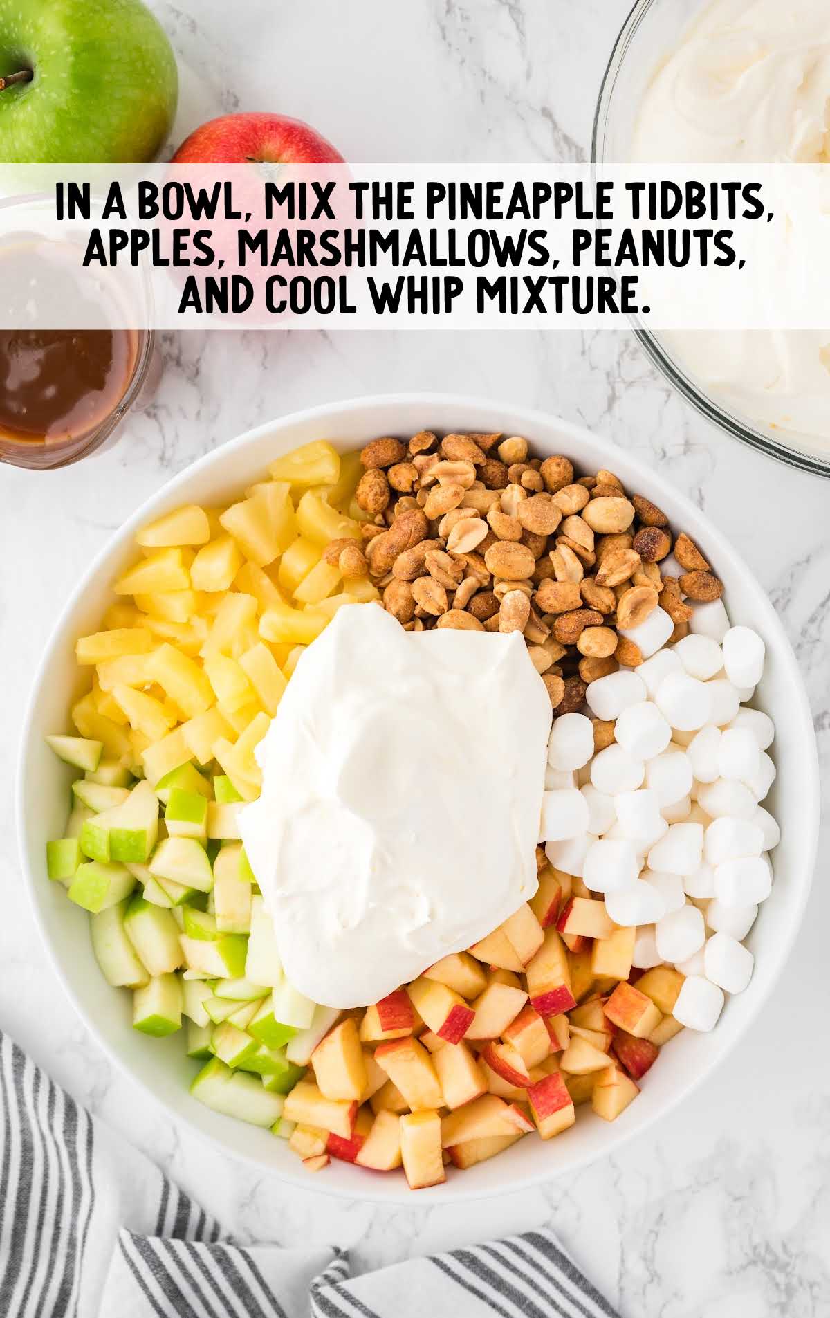 pineapple tidbits, apples, marshmallows, peanuts, and cool whip mixture mixed in a bowl