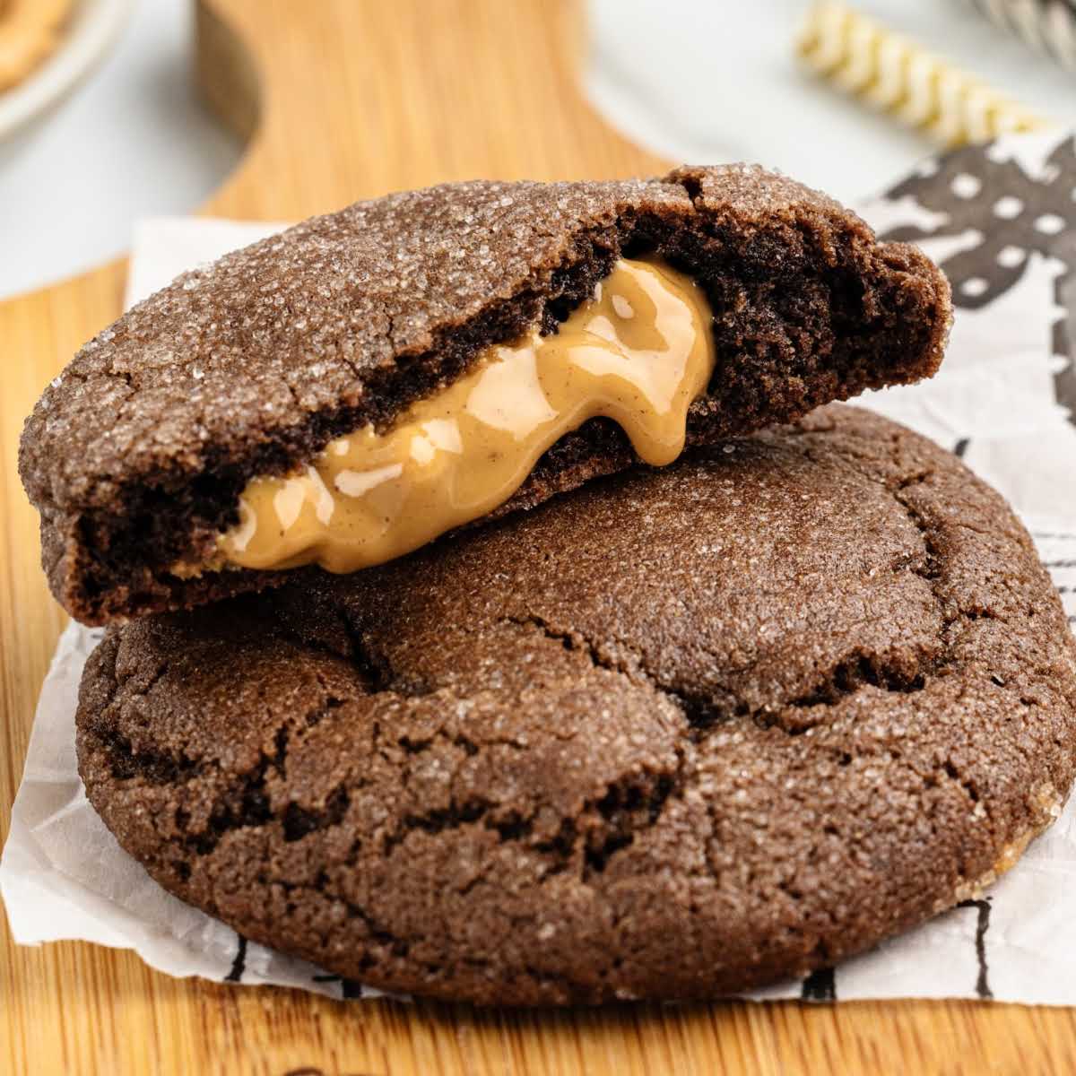 Flat lay of three peanut butter stuffed cookies on parchment paper with one cookie broken to expose the filling.