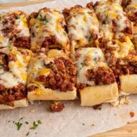 Sliced French bread topped with seasoned ground beef, gooey melted cheese, and chopped herbs, these Garlic Bread Sloppy Joes are beautifully arranged on parchment paper for an irresistible twist on a classic favorite.