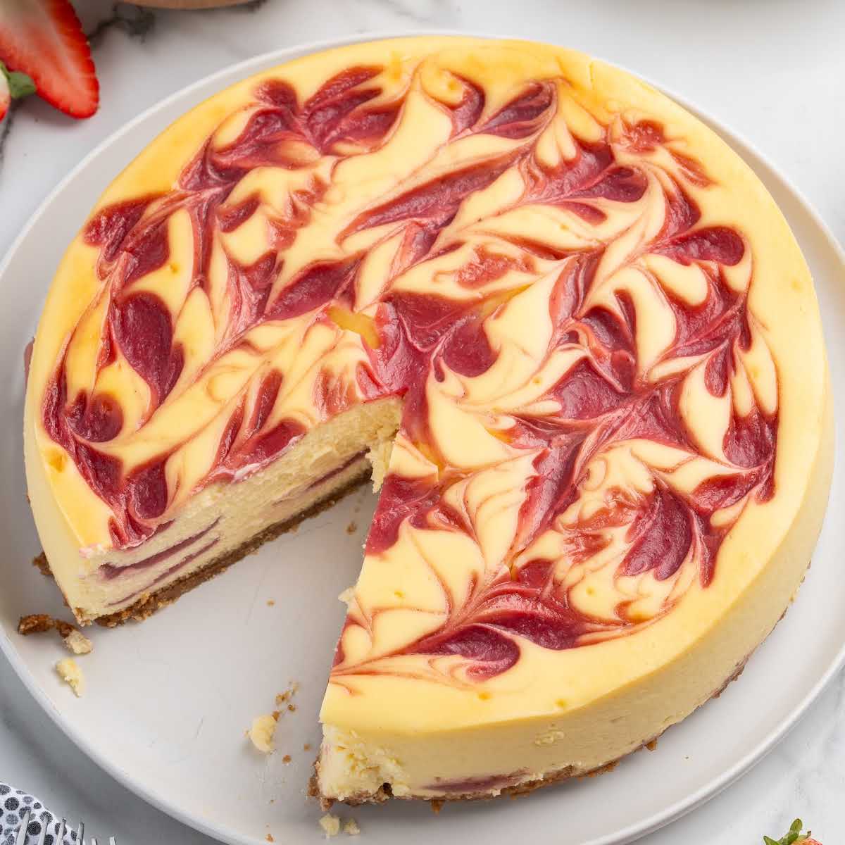 Baked strawberry swirl cheesecake with creamy filling, marbled strawberry topping, and graham cracker crust, sliced on a serving plate