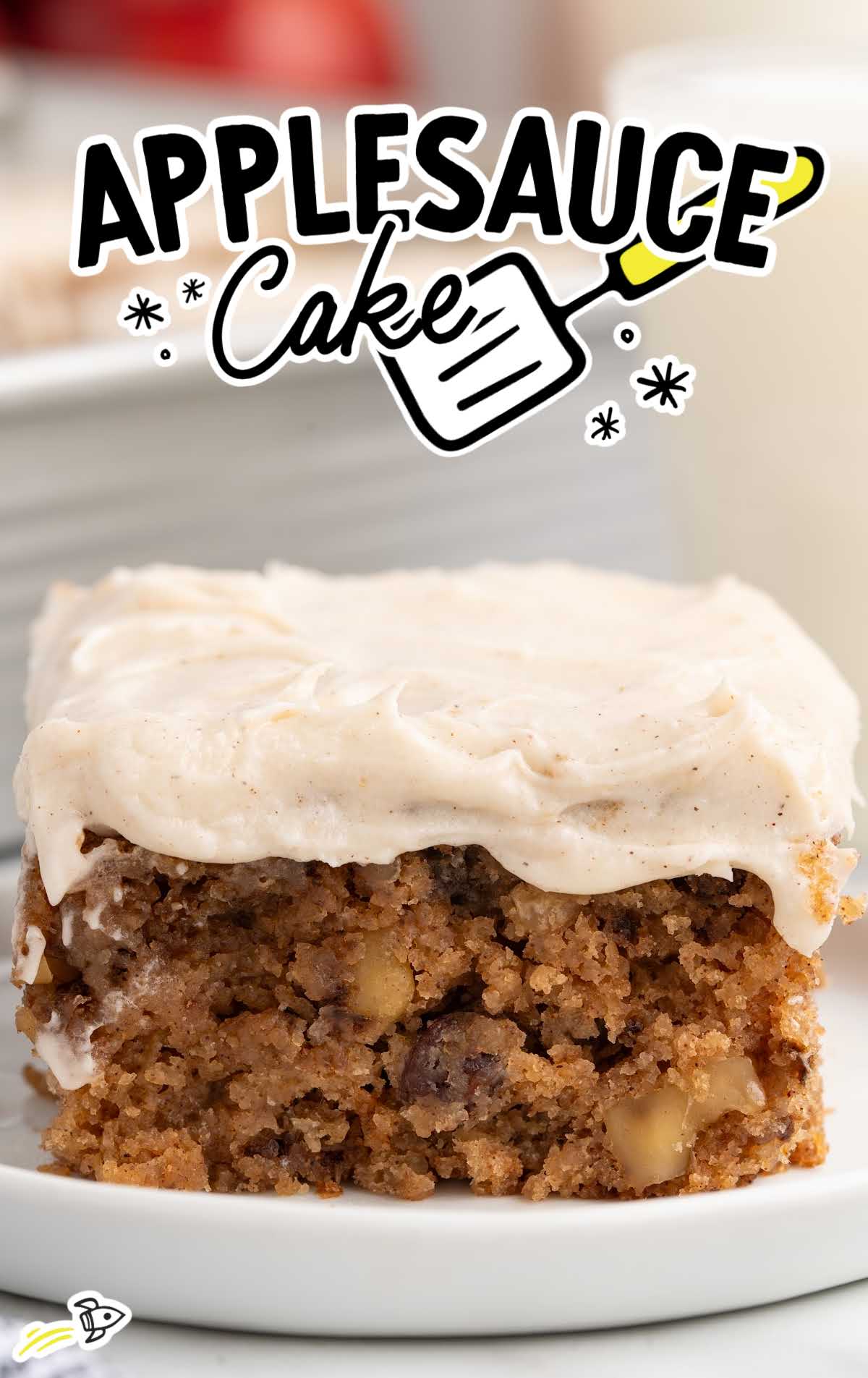 Close-up of applesauce cake square showing fluffy texture with walnuts and raisins under frosting