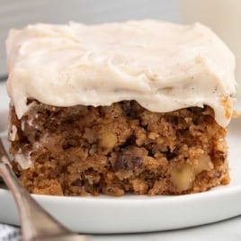 Moist slice of applesauce cake with nuts and raisins topped with creamy frosting on a plate