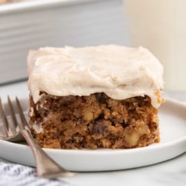 Slice of applesauce cake with walnuts and raisins topped with cream cheese frosting on a small plate