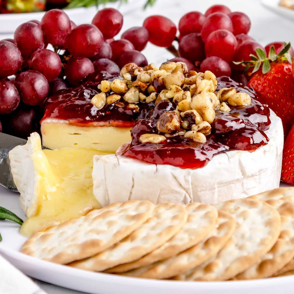 close shot of Baked Brie topped with Jam and walnuts served with crackers