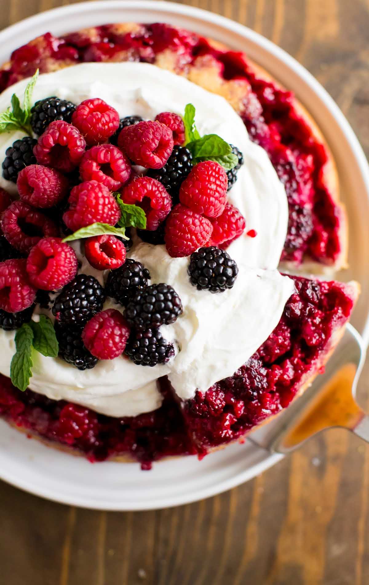 overhead shot of a berry cake topped with whipped cream, berries, and mint