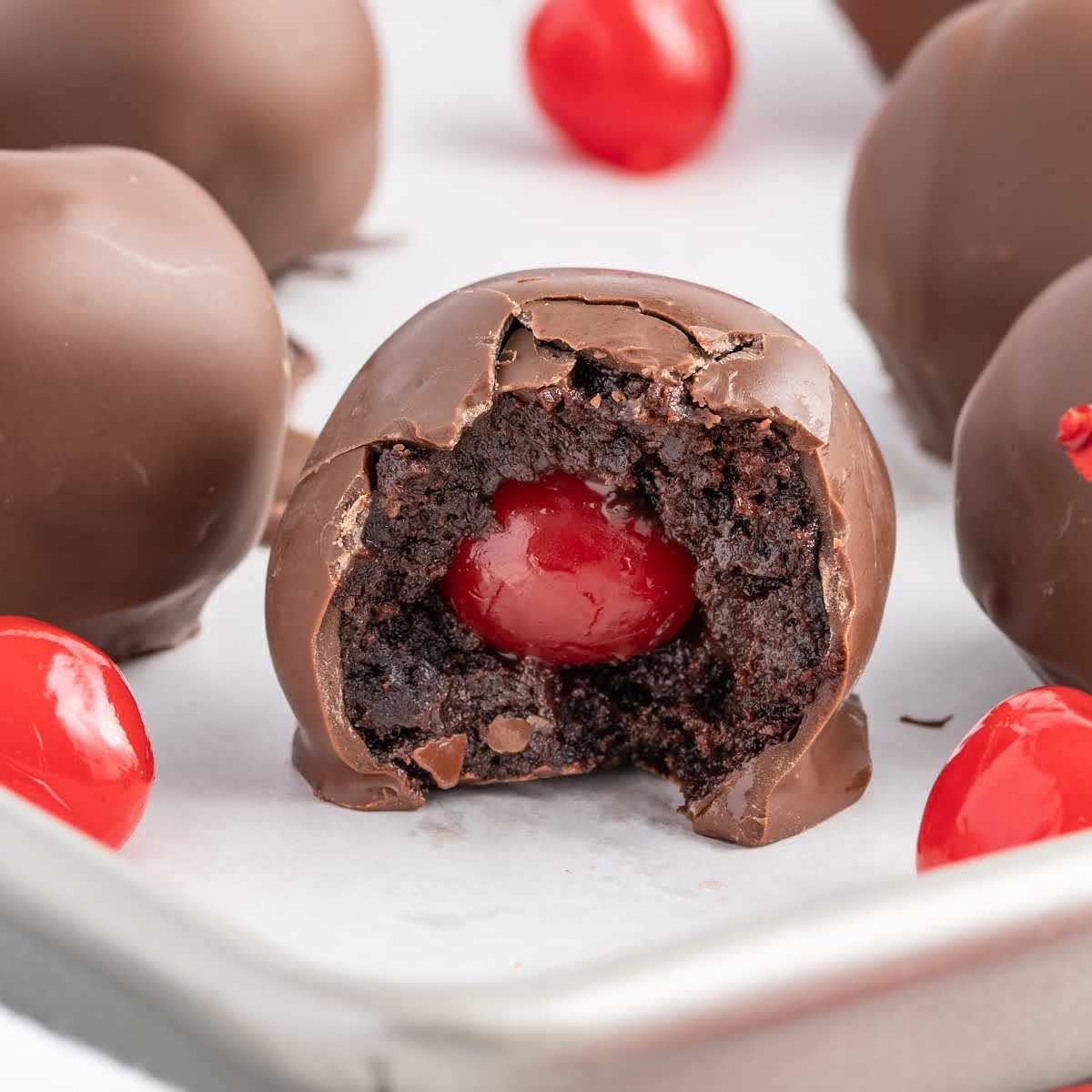 close up shot of a plate of Chocolate Covered Cherry Brownie Bombs with a bite taken out of one of the brownie bombs