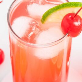 a close up shot of a tall glass of Dirty Shirley Drink garnished with a cherry and a slice of lime