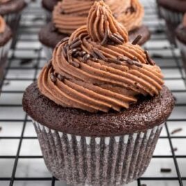 close up shot of a frosted Moist Chocolate Cupcakes topped with chocolate sprinkles on a cooling rack