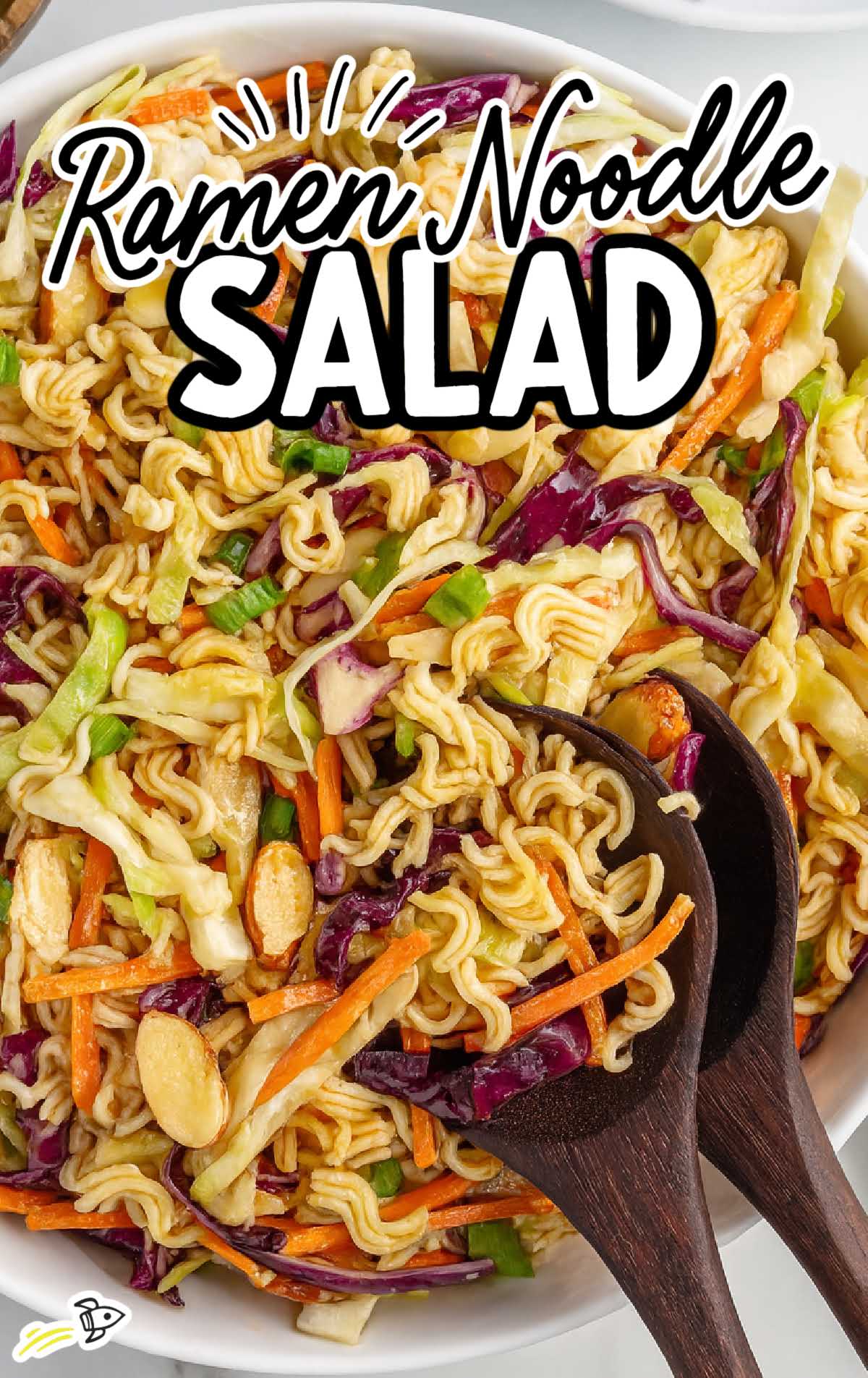 Close-up of ramen noodle salad with red and green cabbage, matchstick carrots, and wooden serving spoons