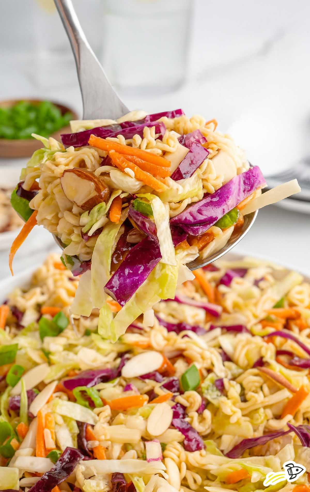 Spoonful of ramen noodle salad showing crunchy vegetables and toasted noodles held above serving bowl