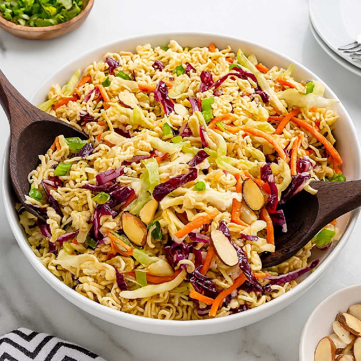 Bowl of ramen noodle salad with carrots, red cabbage, almonds, and green onions served with wooden spoons