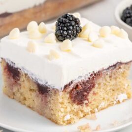 a close-up shot of a slice of White Chocolate Blackberry Poke Cake on a cake