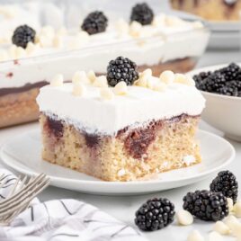 a close-up shot of a slice of White Chocolate Blackberry Poke Cake on a plate