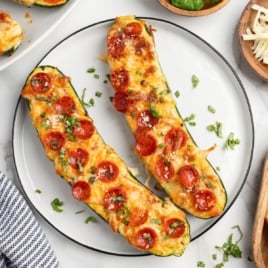 Pizza Zucchini Boats: Two zucchini halves stuffed with melted cheese and mini pepperoni slices, garnished with chopped herbs, served on a white plate.