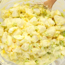 Amish Potato Salad in a bowl with a large wooden spoon
