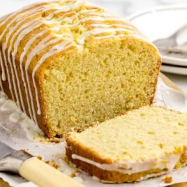 a loaf of lemon cake drizzled with glaze and a slice cut out on a wooden board
