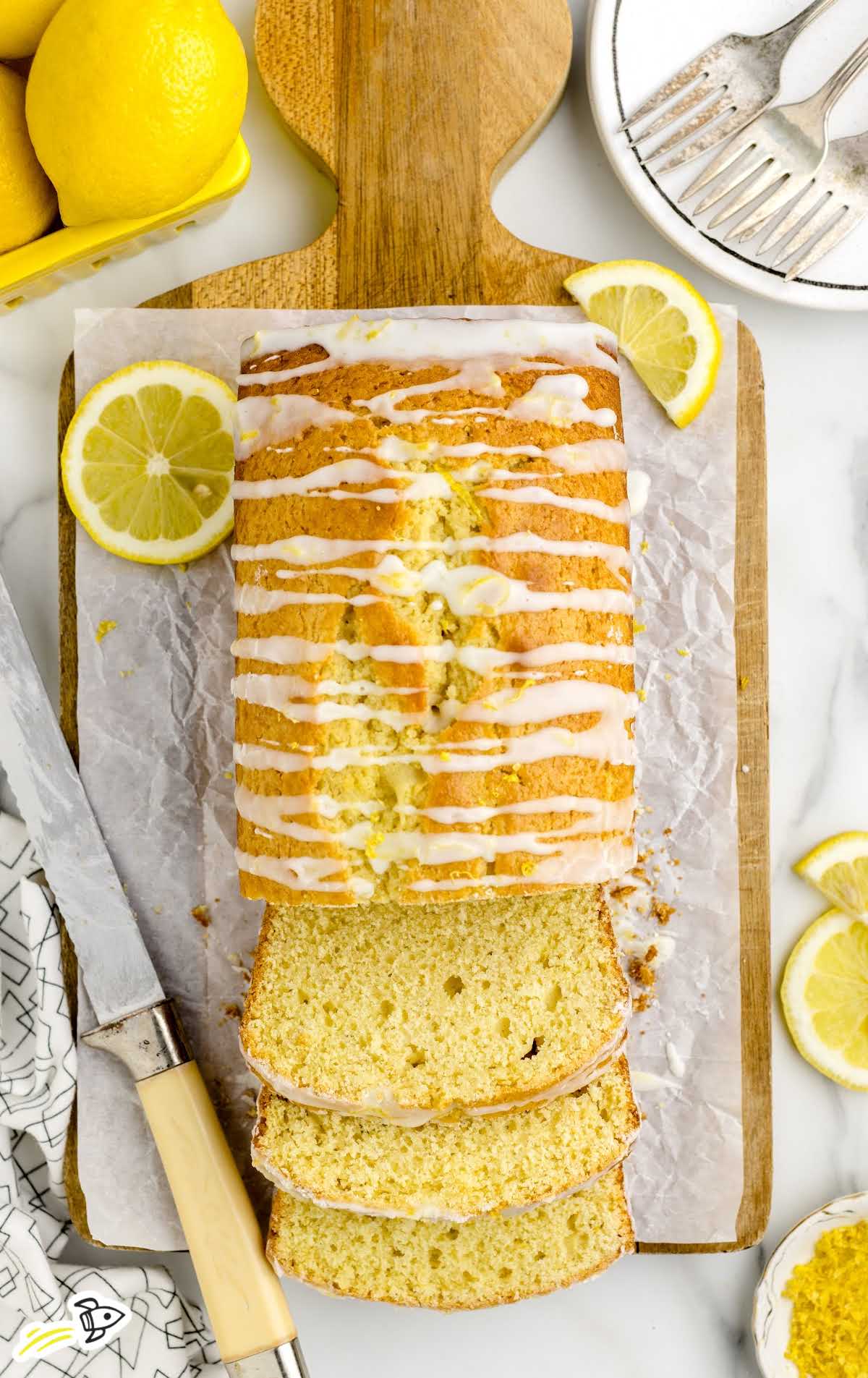 overhead shot of a a loaf of lemon cake drizzled with glaze and slices cut out on a wooden board