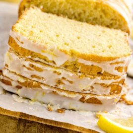 a loaf of lemon cake drizzled with glaze and a slice cut out on a wooden board