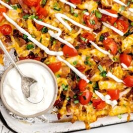 overhead shot of Loaded Fries on a baking tray with a side of sour cream