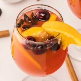 close up shot of a Spiked Apple Cider topped with cranberries and a slice of orange