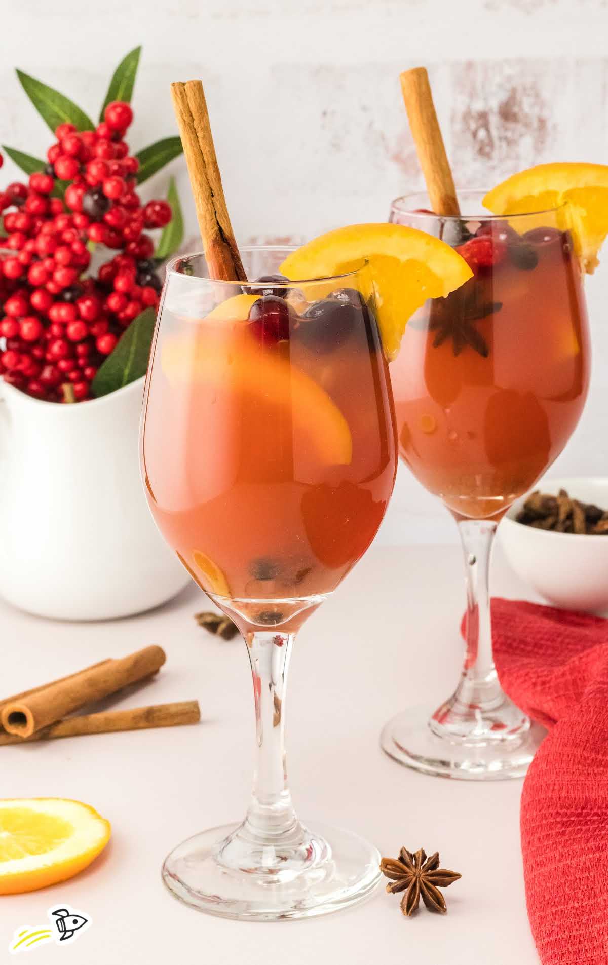 close up shot of multiple Spiked Apple Cider topped with cranberries and a slice of orange