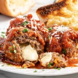 close up shot of Cheese Stuffed Meatballs on a plate with one having a bite taken out of it with a side of garlic bread
