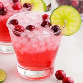 glasses of Cranberry Cocktails garnished with cranberries and a slice of lime on the rim