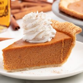 a close up shot of a slice of Fireball Pumpkin Pie on a plate topped with whipped cream on a plate