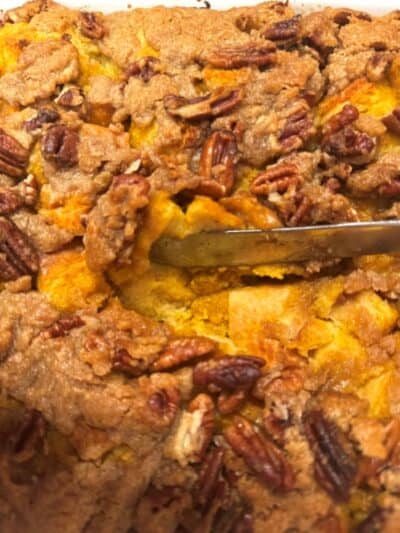 Close-up of a Pumpkin French Toast Casserole with brown streusel topping and pecans, showing a knife cutting into the soft, golden interior.