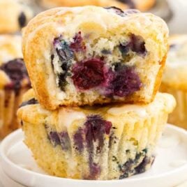 close up shot of a Lemon Blueberry Muffin stacked on another muffin with a bite taken out of it on a plate