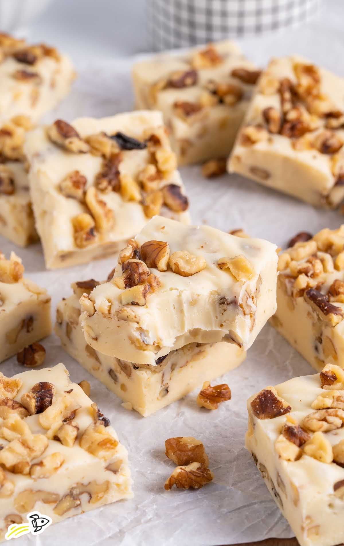 close up shot of Maple Walnut Fudge stacked on top of each other with one having a bite taken out of it.