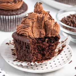 A moist chocolate cupcake on a white plate with a bite out of it. It looks really moist and flavorful.