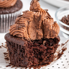 An ultra moist chocolate cupcake on a white plate with a big bite out of it.